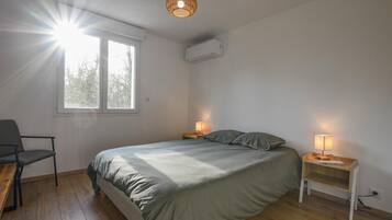 Een slaapkamer met een bed, twee nachtkastjes met lampen, een stoel, een raam en een airconditioning.
