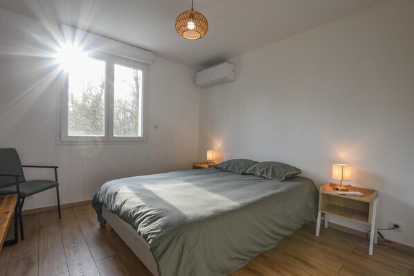 A bedroom with a bed, two bedside tables with lamps, a chair, a window, and an air conditioning unit. - The House of Viennes (SAINT ANDRE LES VERGERS)