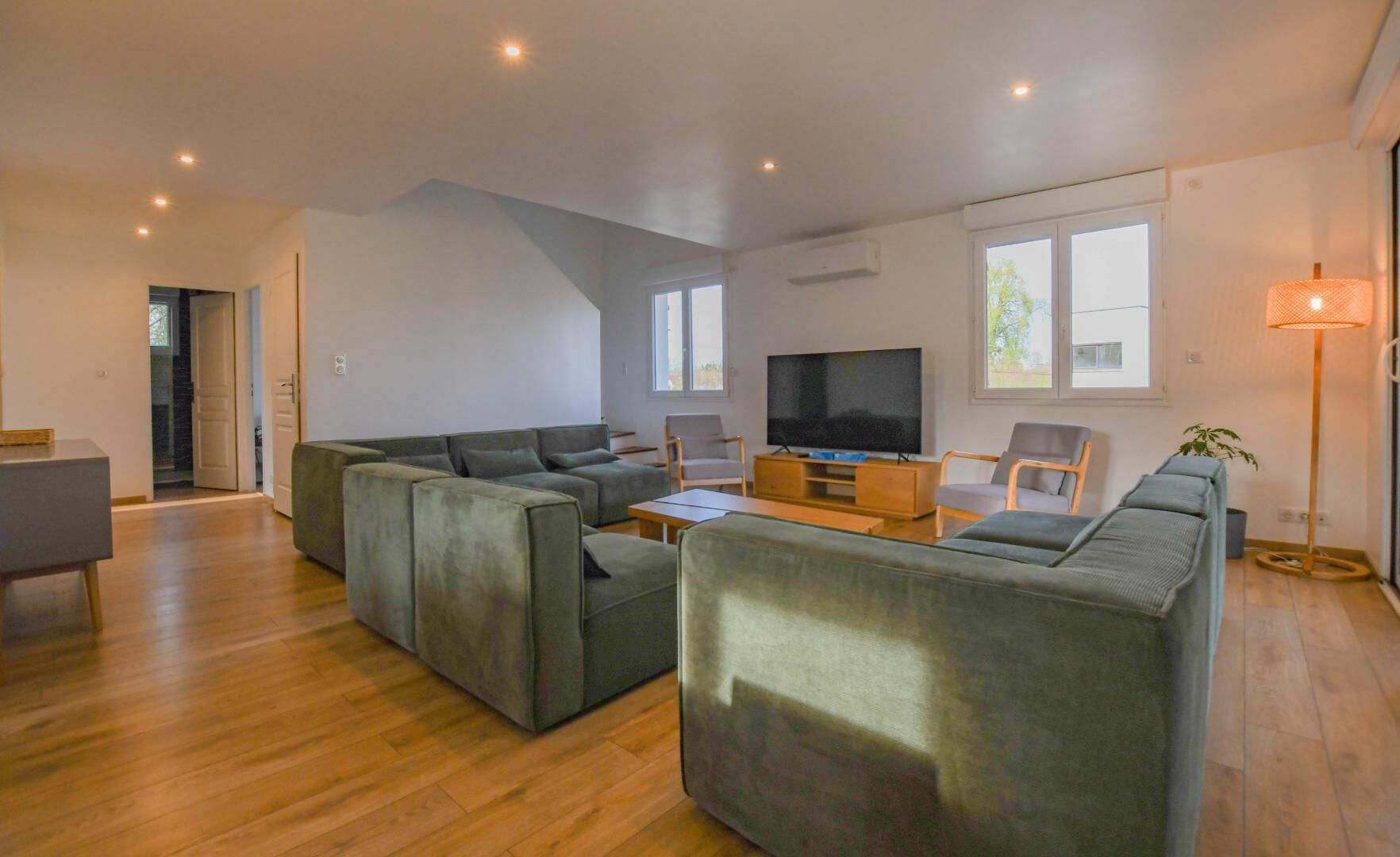 Een moderne woonkamer met een modulaire bank, een flatscreen televisie en een eethoek met een tafel en stoelen.