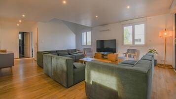 Een moderne woonkamer met een modulaire bank, een flatscreen televisie en een eethoek met een tafel en stoelen.