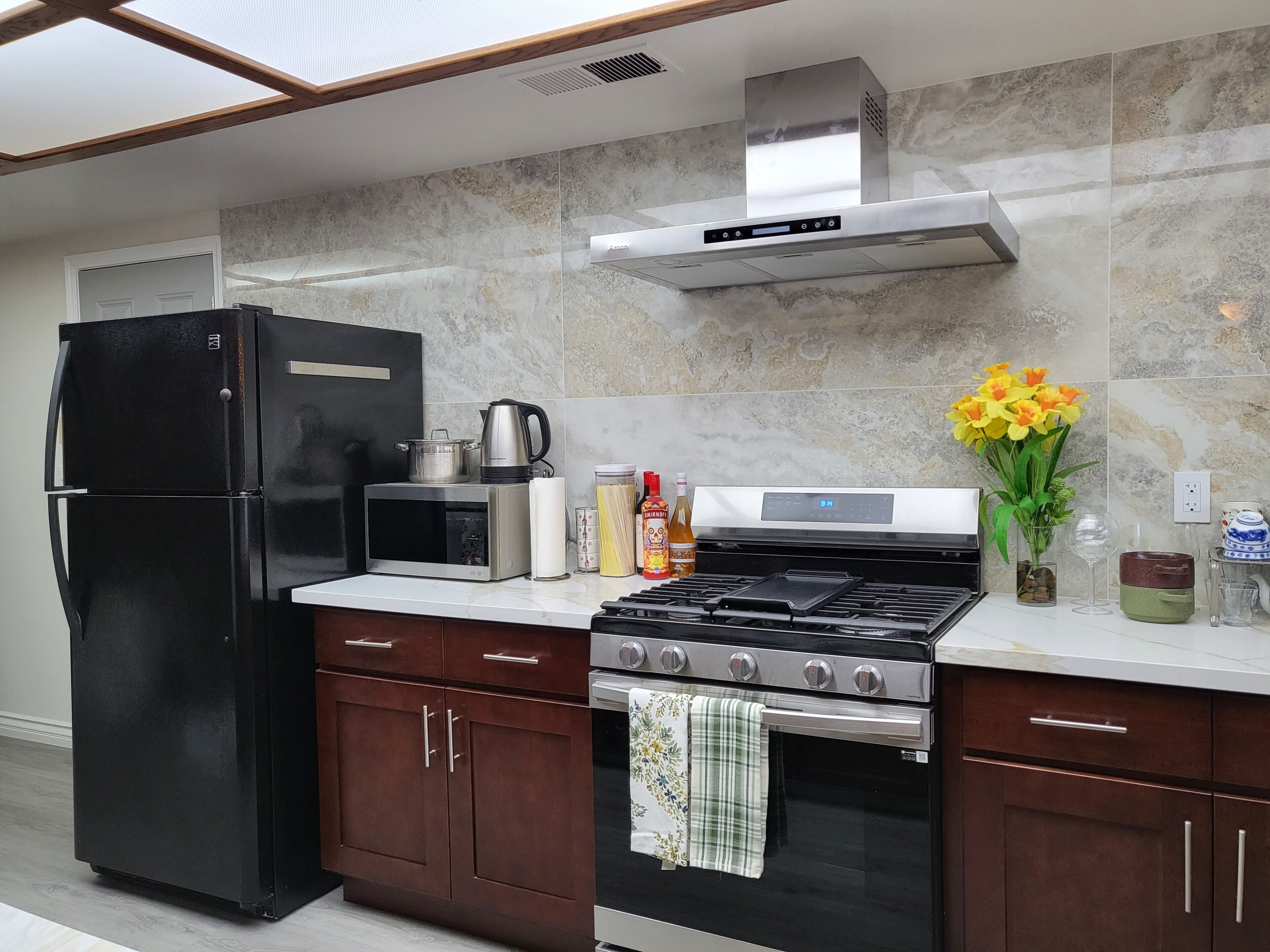 A modern kitchen with a black refrigerator, a microwave, a stove, and a range hood.