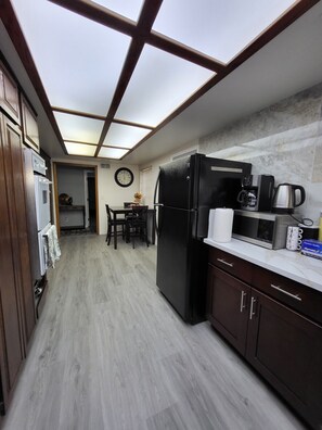 A kitchen with a built-in microwave, a refrigerator, and a coffee maker on the countertop. - Spacious House near Disney/Knott's (La Mirada)