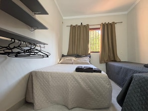 A bedroom with a bed, a bedside table, a hanging clothes rack, and a window with curtains.