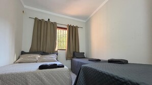 Una habitación con dos camas, cada una con edredón acolchado, una ventana con cortinas y una pared visible.