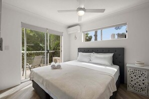 Ein Schlafzimmer mit einem großen Bett, einem Deckenventilator, einem Fenster mit Blick und einer Glastür, die zu einem Außenbereich führt.