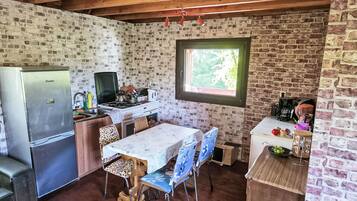 Een landelijke keuken met een bakstenen muur, houten balkenplafond, een eettafel met stoelen, een koelkast, een fornuis en een raam.