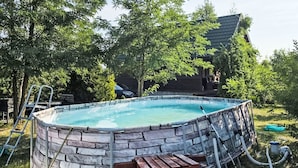 Piscina circular com exterior de pedra, rodeada por relva e árvores.