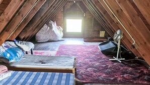 Quarto de sótão pequeno com duas camas, um ventilador e uma janela que oferece luz natural.