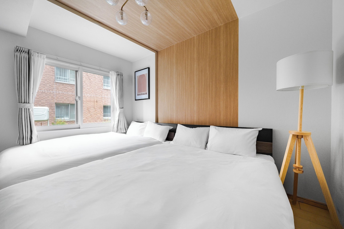 A hotel room with two beds, a large window, a framed picture on the wall, and a floor lamp.