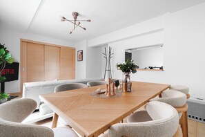A modern dining area with a wooden table, grey upholstered chairs, a ceiling light fixture, and a plant on the table. - E-US NAEBO STATION 101 (Sapporo)