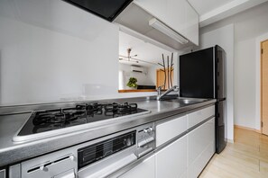 A modern kitchen with a gas stove, stainless steel appliances, and a black refrigerator. - E-US NAEBO STATION 101 (Sapporo)
