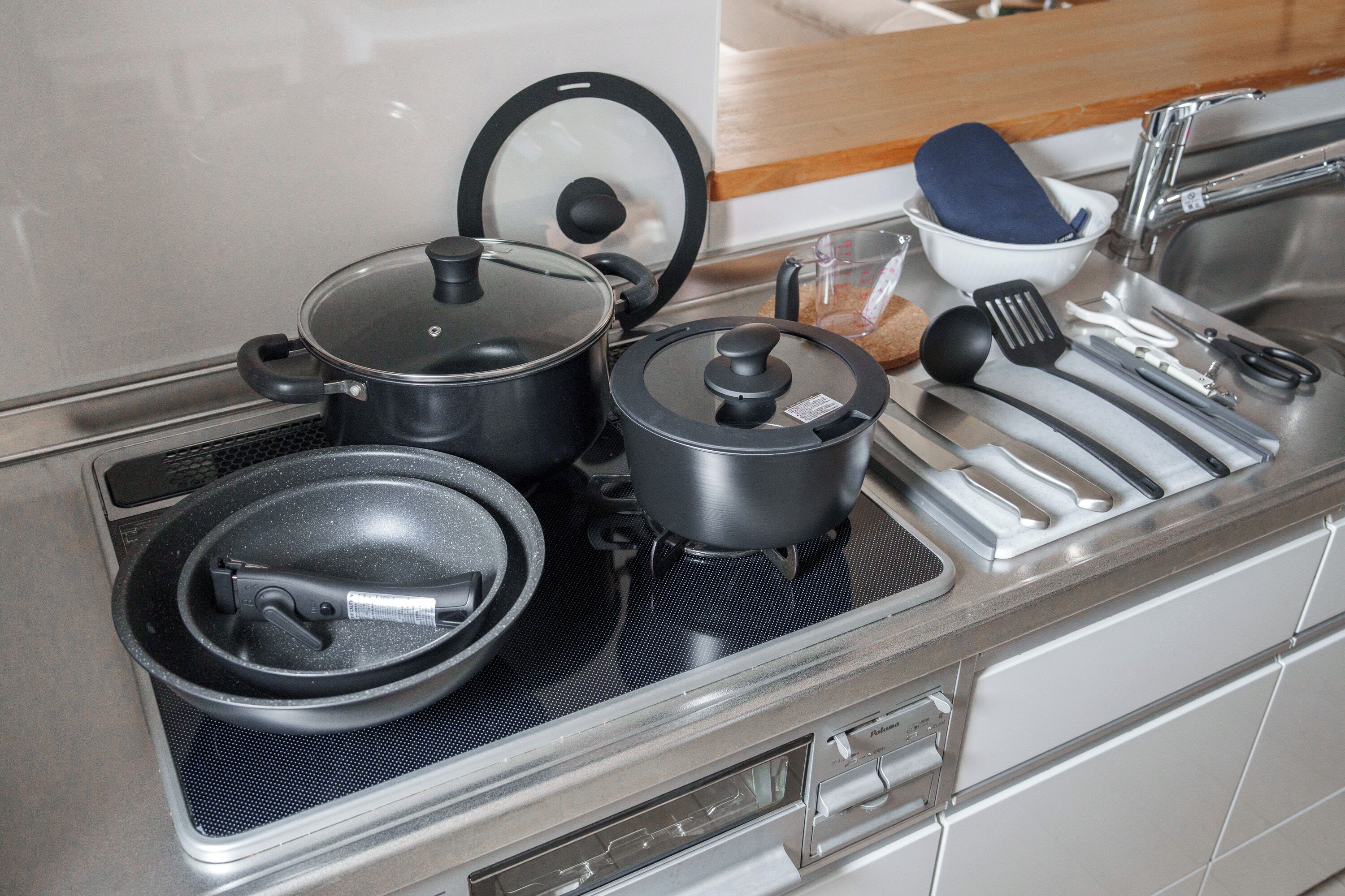 Una cocina con estufa, ollas, sartenes, una sartén, una espátula y una taza medidora.