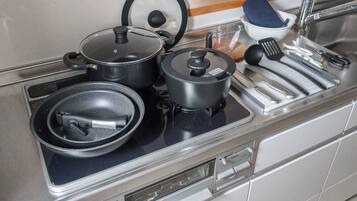 Una cocina con estufa, ollas, sartenes, una sartén, una espátula y una taza medidora.