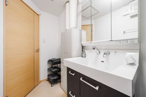 A bathroom with a white sink, a mirror, a towel rack, and a door. - E-US NAEBO STATION 101 (Sapporo)
