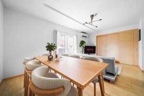 A modern living space with a wooden dining table, cushioned chairs, a grey sofa, and a television displaying 'NETFLIX'. - E-US NAEBO STATION 101 (Sapporo)