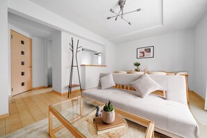 A modern living room with a glass coffee table, a sofa with cushions, a wooden door, and a ceiling light fixture. - E-US NAEBO STATION 101 (Sapporo)