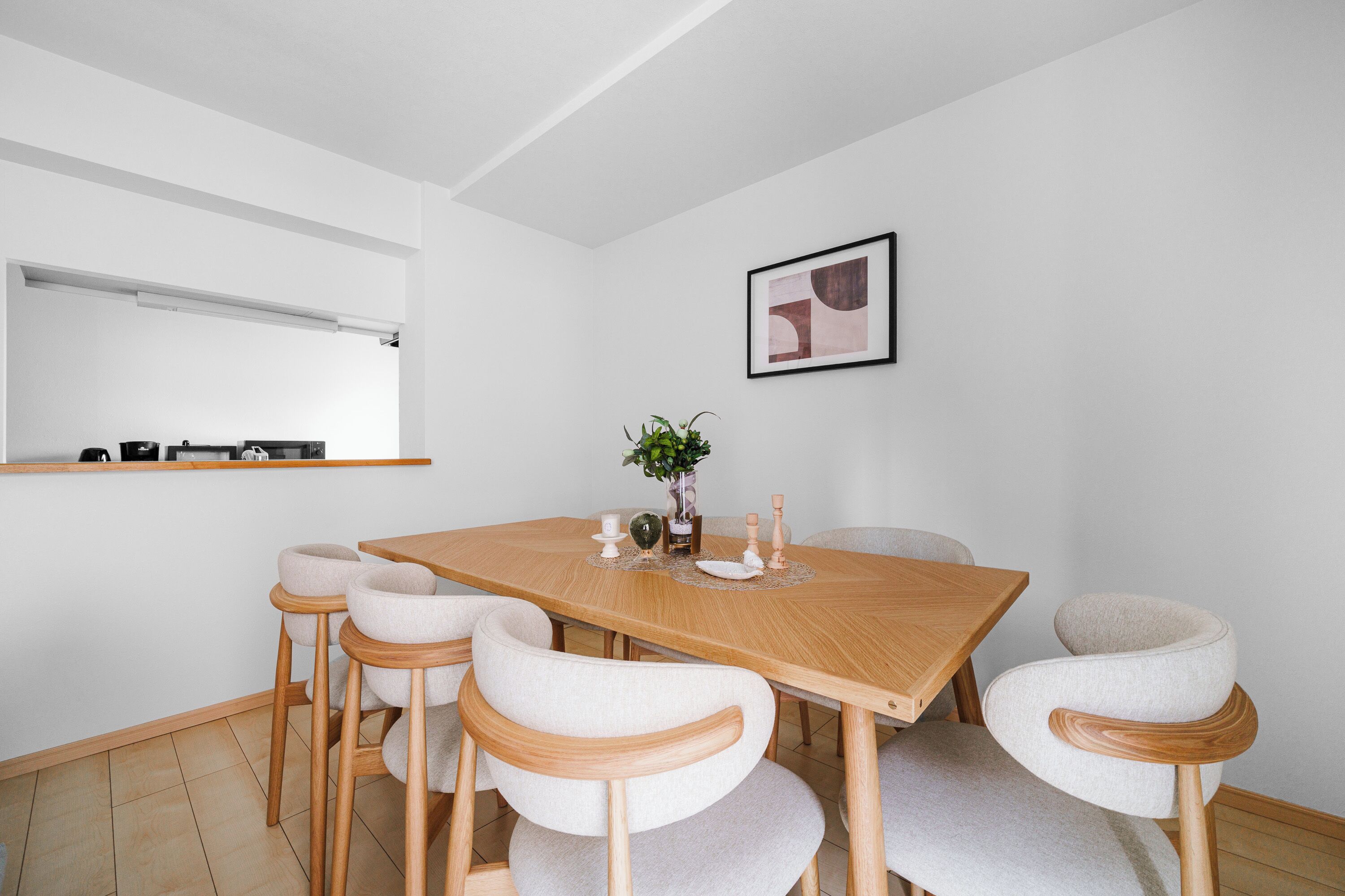 Un comedor moderno con una mesa de madera, seis sillas tapizadas, una planta en maceta y una obra de arte abstracta enmarcada en la pared.
