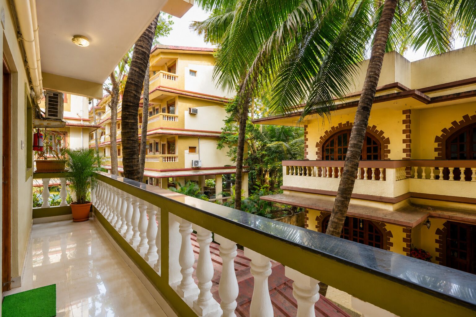 A multi-story building with balconies, palm trees, and a tiled floor.