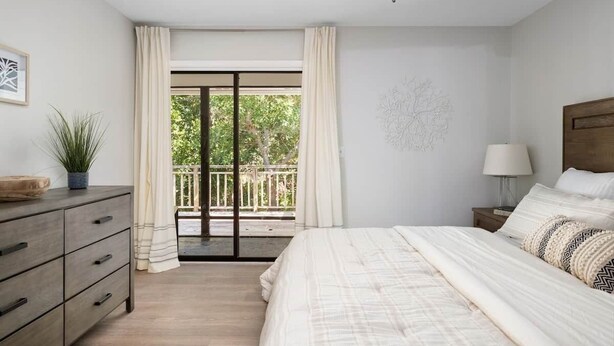 Un dormitorio con cama, cómoda, mesita de noche, lámpara y vistas a un balcón con barandilla.
