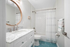 A bathroom with a white sink, a mirror, a toilet, and a shower with a curtain. - Palmetto Place | Beach, Pool & Walkable Dining (Vero Beach)