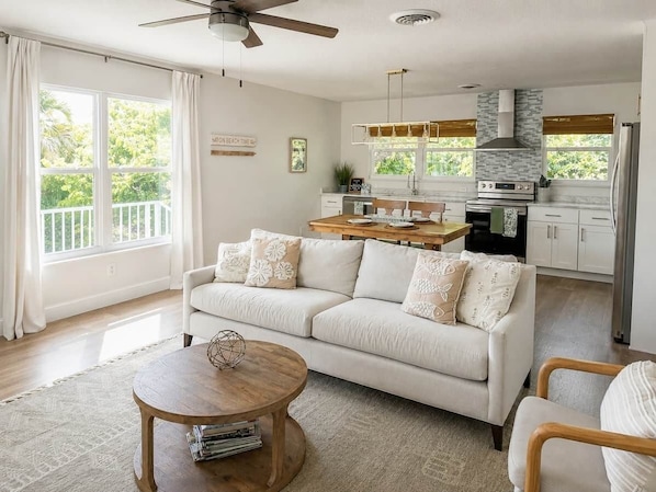 A modern living room with a sofa, a coffee table, and a kitchen in the background. - Palmetto Place | Beach, Pool & Walkable Dining (Vero Beach)