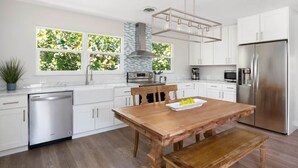 Una cocina moderna con armarios blancos, un refrigerador de acero inoxidable, una mesa de comedor de madera y un lavavajillas integrado.