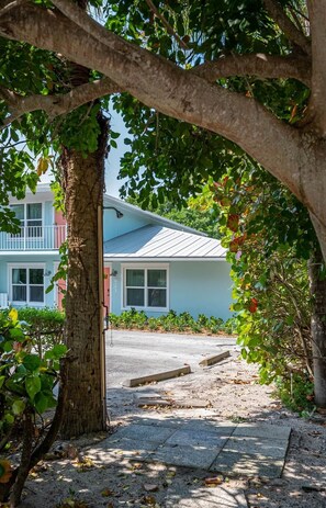 A residential building with a visible front porch, a tree in the foreground, and a clear view of the street. - Palmetto Place | Beach, Pool & Walkable Dining (Vero Beach)