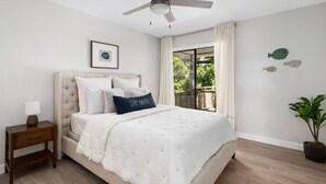 Un dormitorio con cama, mesita de noche, ventilador de techo, ventana con cortinas y una planta en maceta.