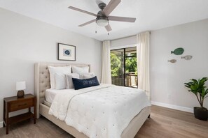 A bedroom with a bed, a nightstand, a ceiling fan, a window with curtains, and a potted plant. - Palmetto Place | Beach, Pool & Walkable Dining (Vero Beach)