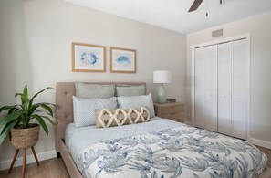 A bedroom with a bed, a nightstand, a lamp, a potted plant, and a wardrobe. - Pineapple Pad: Beach + Pool + Walkable Dining (Vero Beach)