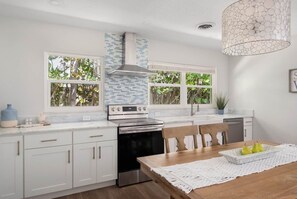 A modern kitchen with white cabinetry, a built-in oven, and a dining area with a wooden table. - Pineapple Pad: Beach + Pool + Walkable Dining (Vero Beach)