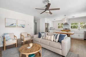 A modern living room with a sofa, chairs, a coffee table, and a ceiling fan. - Pineapple Pad: Beach + Pool + Walkable Dining (Vero Beach)
