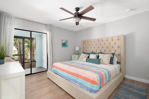 Un dormitorio con una cama grande, un ventilador de techo, una mesita de noche y vistas a través de una puerta corrediza de vidrio.