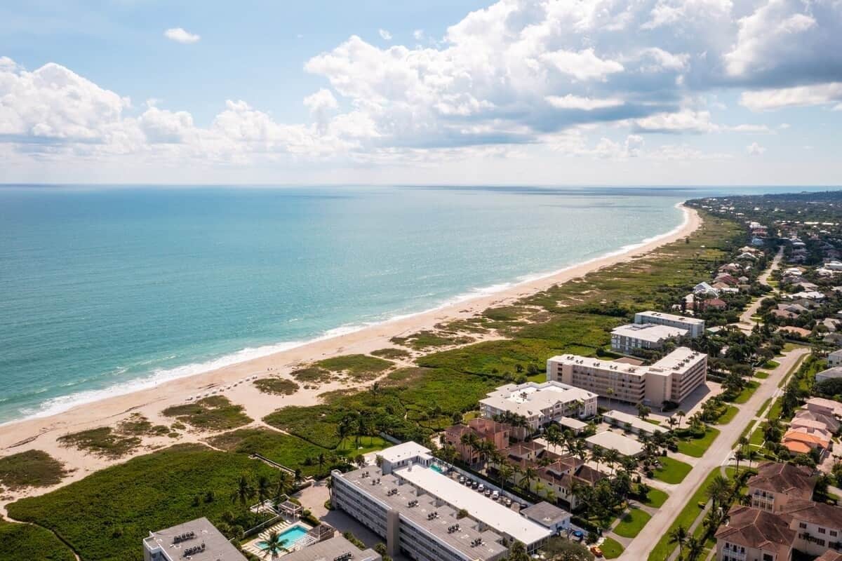 An aerial view of a coastal area with a beach, buildings, and greenery.