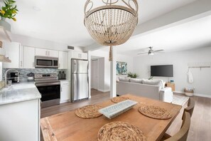 Eine moderne Küche mit Edelstahlgeräten, einem Holzespeisetisch mit Tischsets und einer Pendelleuchte.