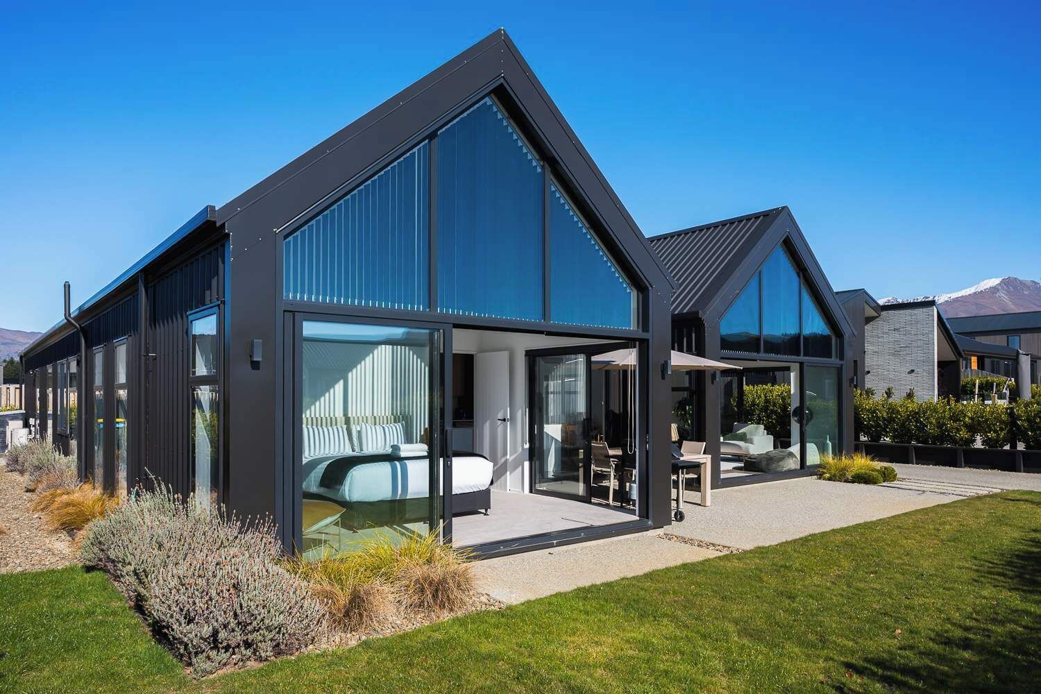 Ein modernes, zweistöckiges Haus mit großen Glasfenstern, einem sichtbaren Schlafzimmer mit Bett und einer Terrassenfläche.