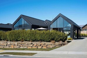 A modern residential building with a stone retaining wall, a clear sky, and a well-maintained lawn.