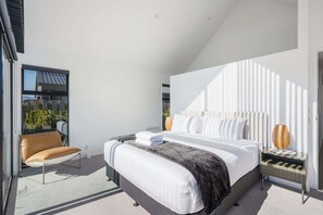 Une chambre moderne avec un grand lit, une chaise, une table de chevet et une fenêtre donnant sur un paysage verdoyant.