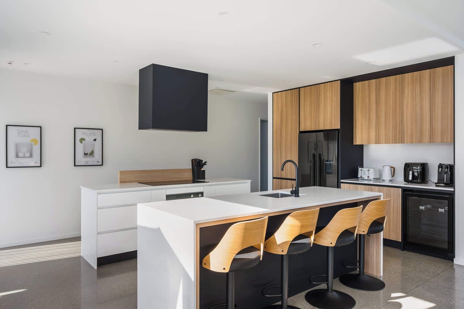 A modern kitchen with a central island, bar stools, a built-in oven, and a refrigerator.
