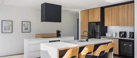 A modern kitchen with a central island, bar stools, a built-in oven, and a refrigerator.
