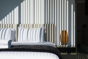 A bed with white bedding and a black accent, a nightstand with a woven lamp, and a wall with vertical slats.