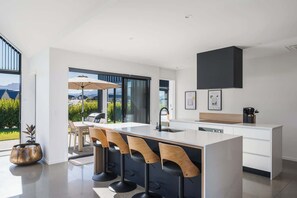 Une cuisine moderne dotée d’un grand îlot central, de tabourets de bar et offrant une vue sur l’extérieur.