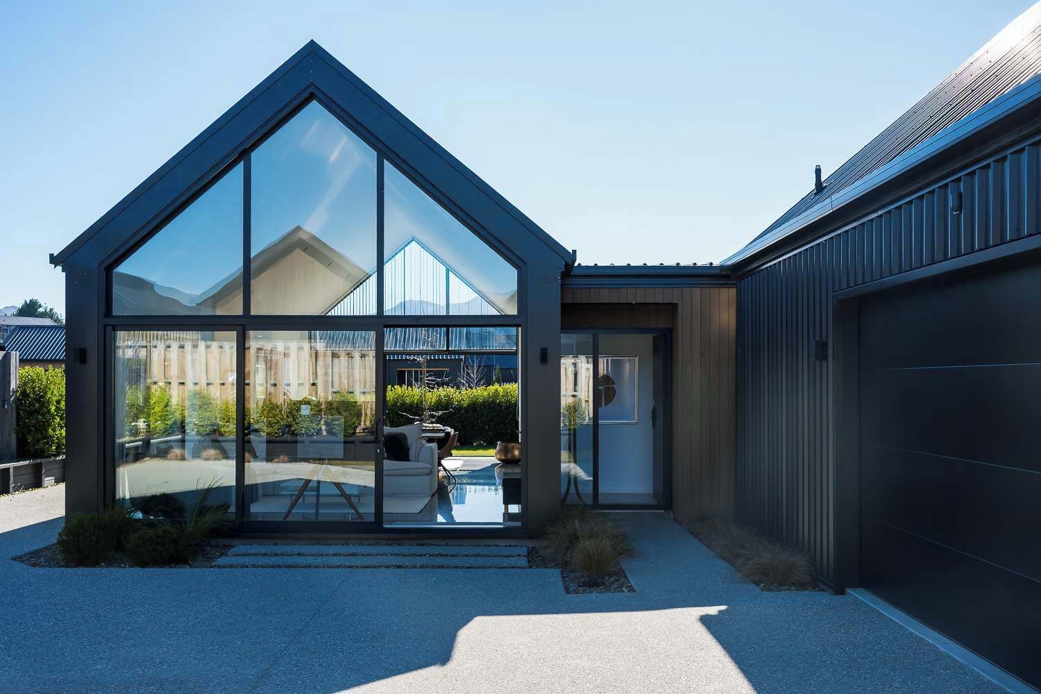 Ein modernes Haus mit großer Glasfassade, einer Garage und einer sichtbaren Außenbereich-Sitzgelegenheit.