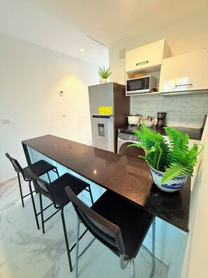 A modern kitchen with a black countertop, two bar stools, a microwave, a coffee maker, and a potted fern. - Penthouse + pool + beach + Hard Rock campus and golf course (Punta Cana)