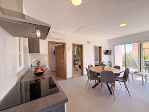A modern kitchen with a black countertop, a dining area with a round table and chairs, and a large window with a view. - Holiday apartment with shared use of pool (Polje/Krk)