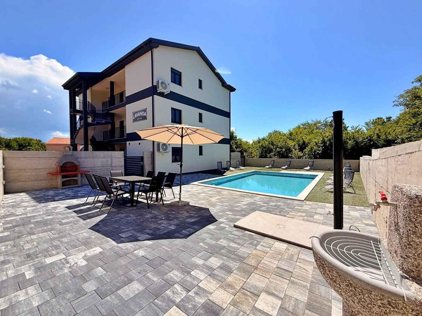 A two-story building with a swimming pool, outdoor seating, and a barbecue area.