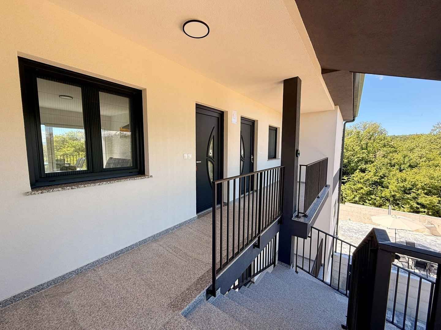 A building exterior with a covered balcony, a staircase, and a view of trees.