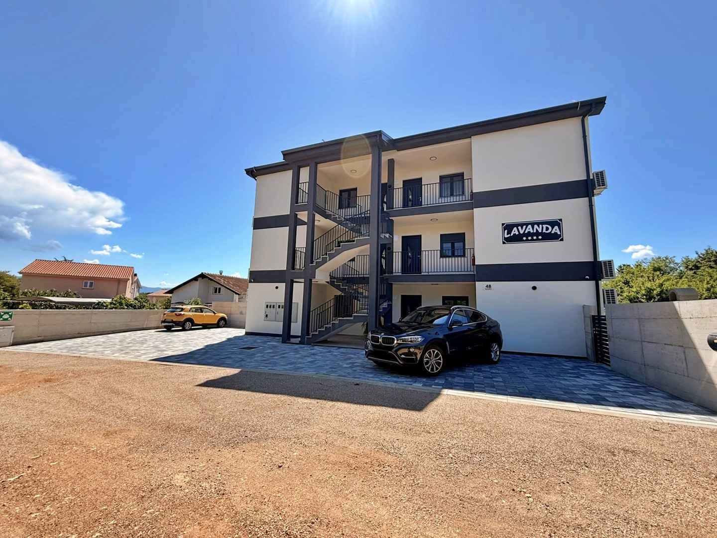 Un edificio de varios pisos con un letrero que dice 'LAVANDA' en la fachada, una escalera que conduce a los pisos superiores y un coche negro estacionado adelante.