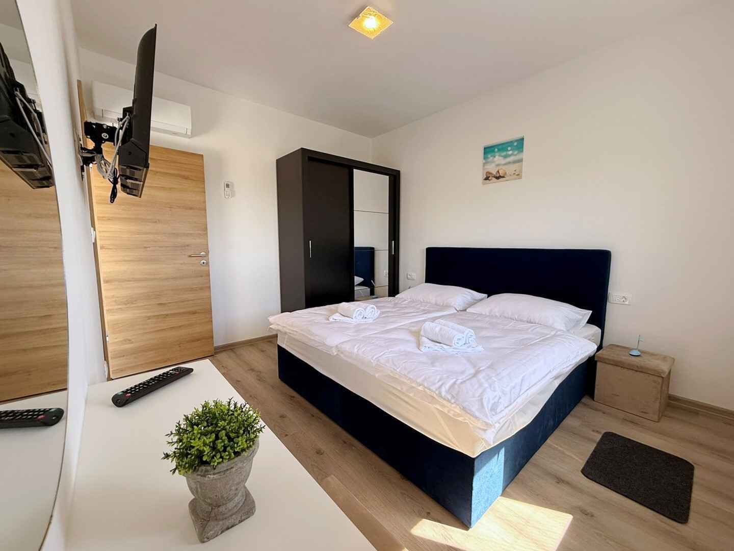 Une chambre à coucher moderne avec un lit, une table de chevet, des télécommandes et une plante en pot.