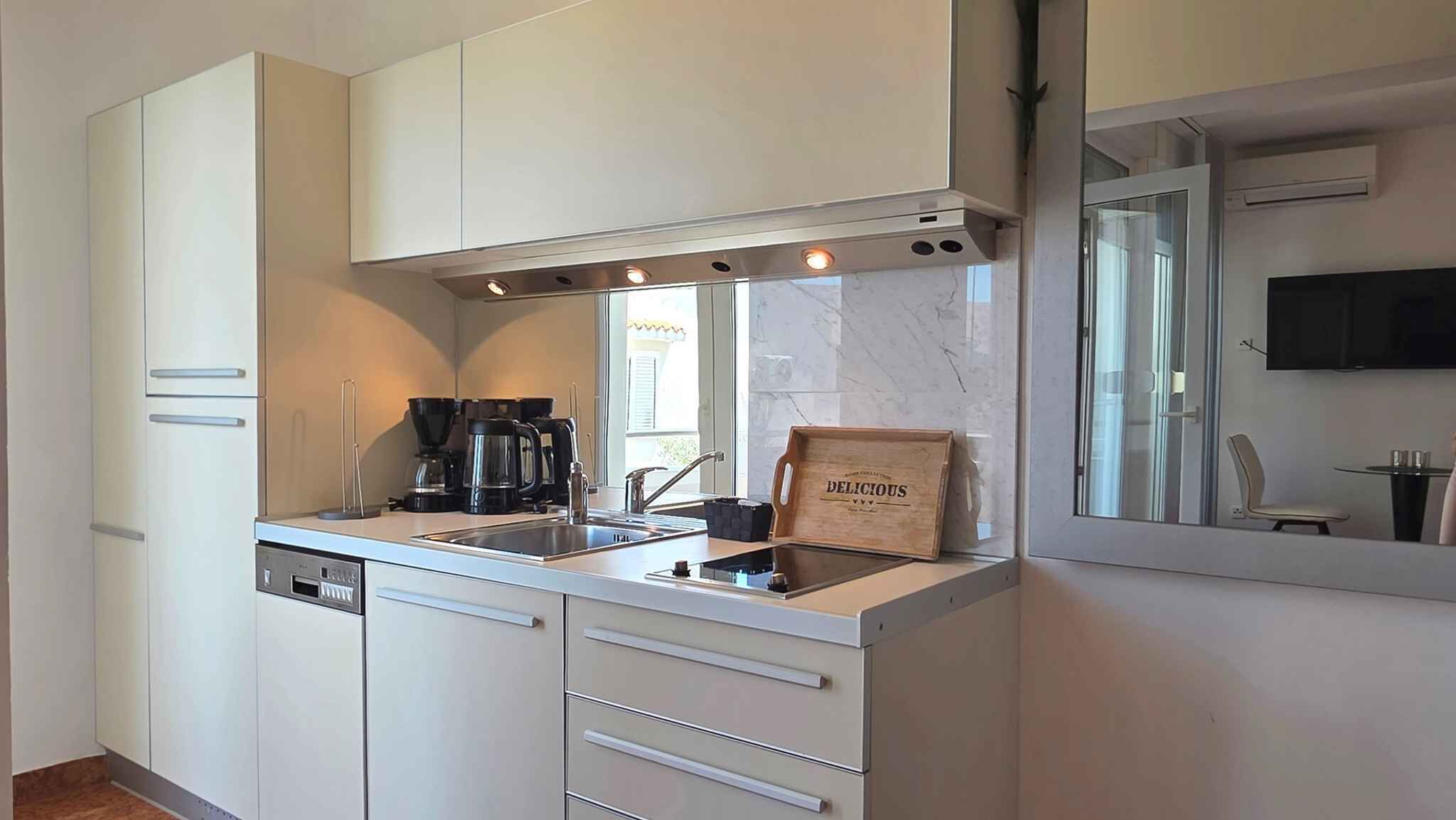 Una cocina moderna con armarios blancos, lavavajillas integrado, cafetera y un letrero de madera en la encimera.